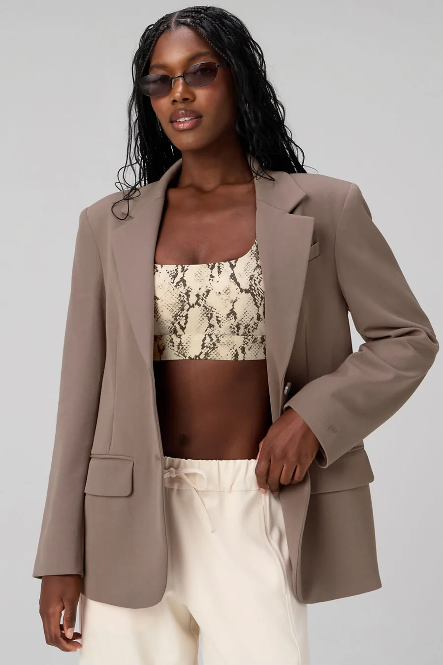 Frau in taupefarbenem Blazer über gemustertem Bustier und cremefarbener Hose