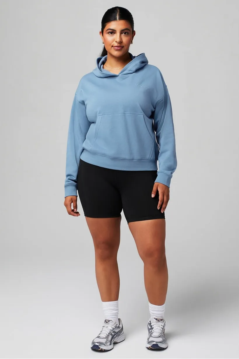 Frau in hellblauem Hoodie und schwarzen Radlershorts, Ganzkörperaufnahme