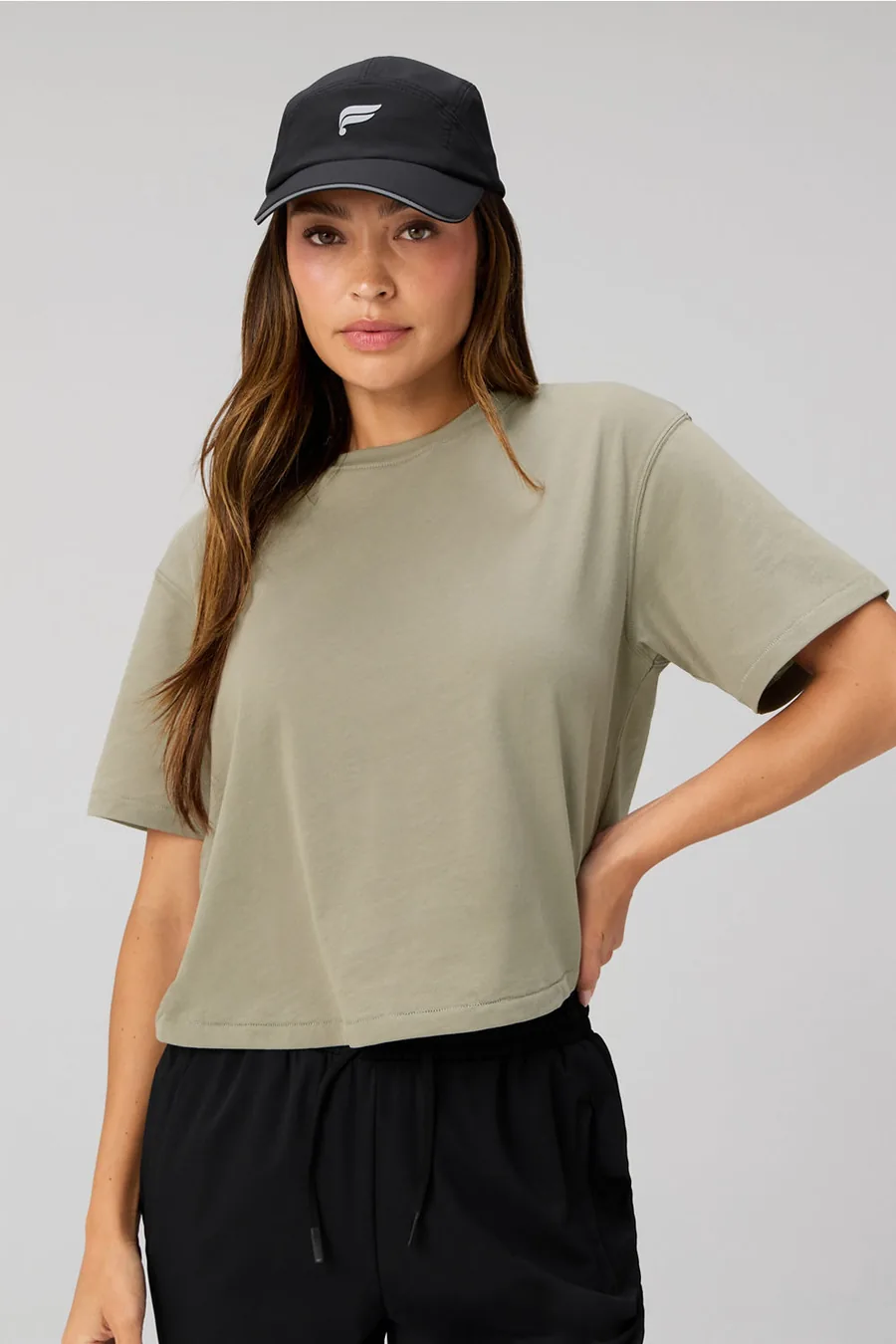 Frau in olivfarbenem T-Shirt, schwarzer Hose und schwarzer Kappe