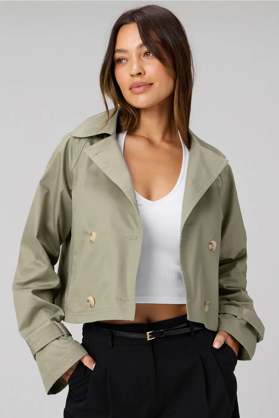 Frau in kurzem olivfarbenem Trenchcoat über weißem Top und schwarzer Hose