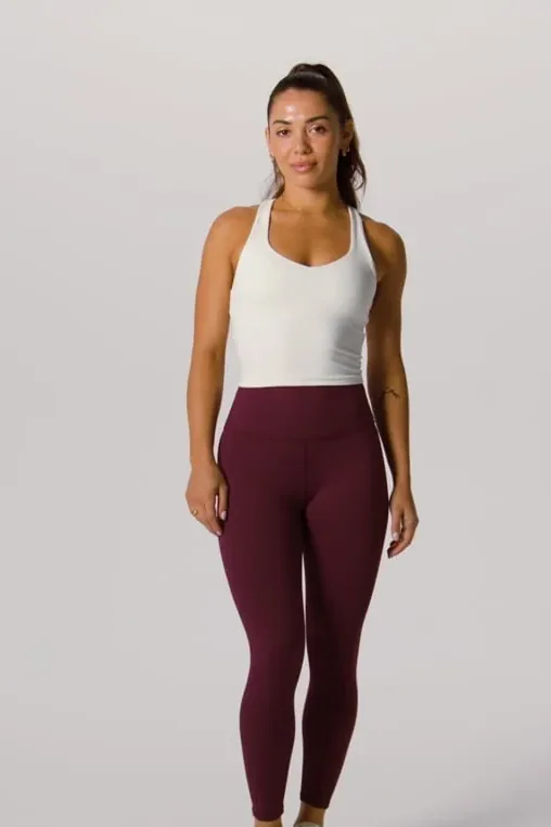 Frau in bordeauxroter Leggings und weißem Top, von Kopf bis Knöchel vor hellgrauem Hintergrund